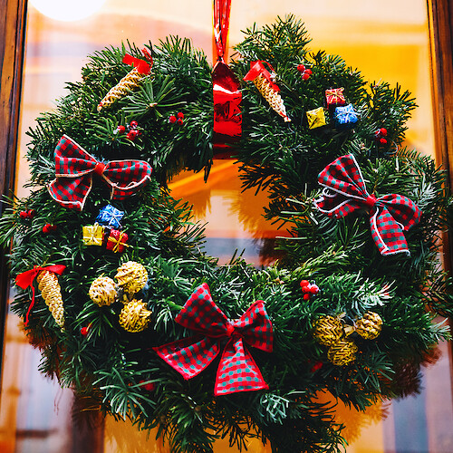 A festive Christmas wreath adorned with red plaid bows, small gifts, pine cones, and berries hangs on a wooden door.