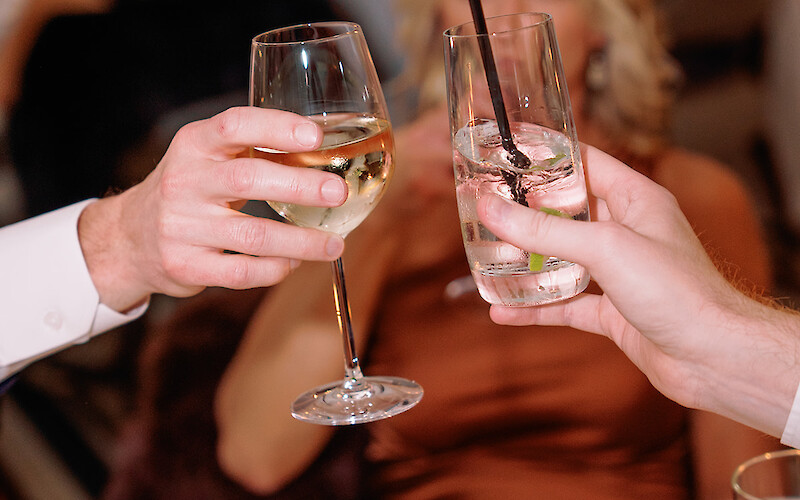 People are clinking glasses at a dining table, with candles and flowers in the background, creating a celebratory atmosphere.