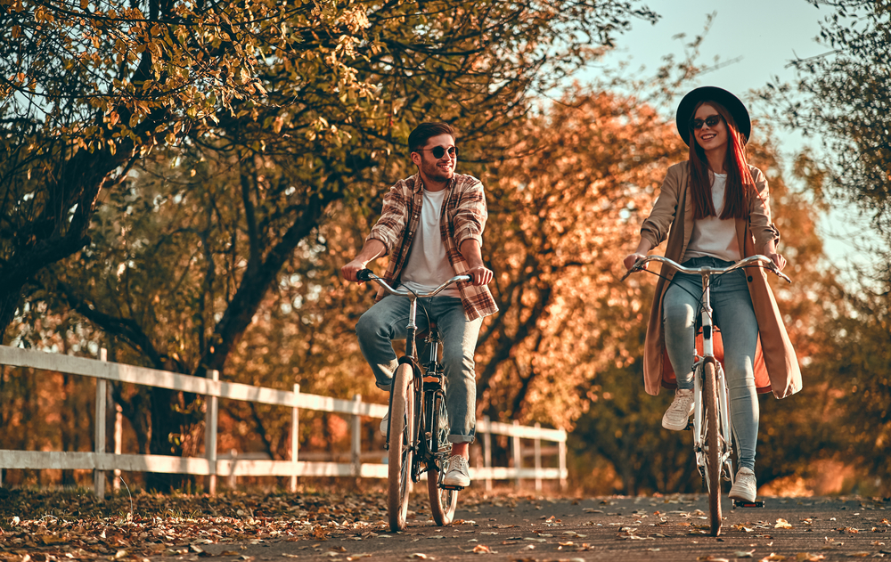 Two people are riding bicycles on a scenic path lined with autumn trees, enjoying a pleasant day together.